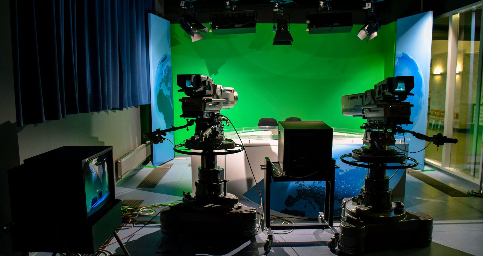 Television studio floor with broadcast cameras in front of a green-screen set