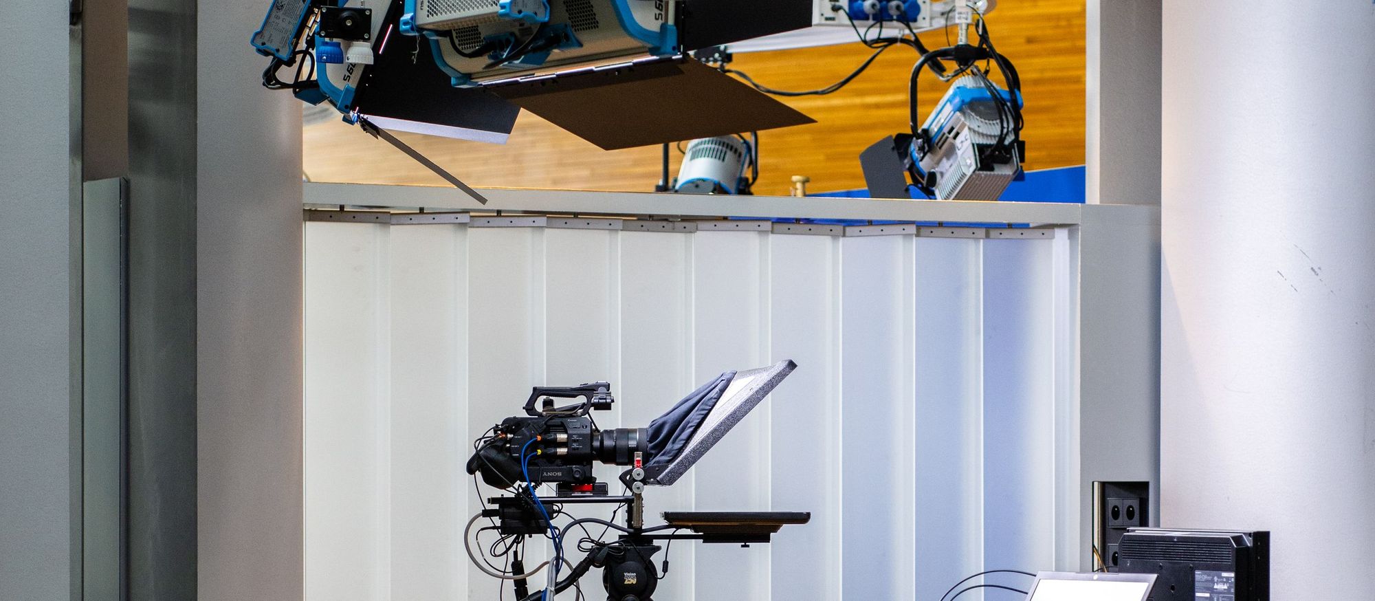 Studio camera on a pedestal with a teleprompter under ceiling-mounted studio lights